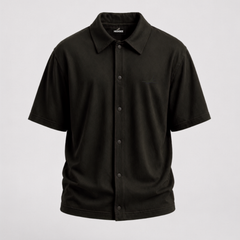 A black short-sleeve button-up camp shirt with a classic collar and a single chest pocket, displayed on a neutral light gray background.