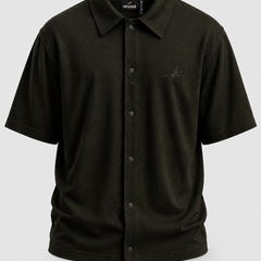 A dark olive green short-sleeve button-up shirt by, 'HEGGEE' featuring a classic collar, snap-button front, and a small embroidered logo on the left chest, displayed on a neutral light gray background.