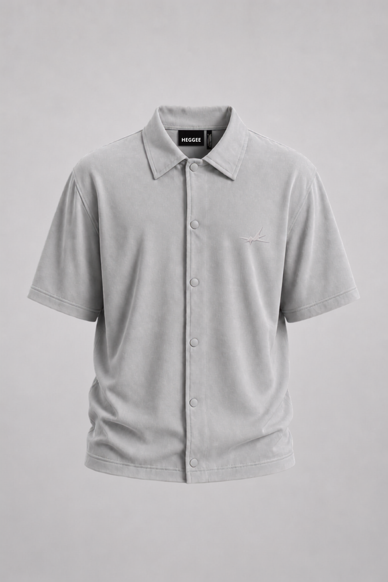 A light gray short-sleeve button-up shirt with a classic collar and a small embroidered logo on the left chest, displayed on a neutral gray background.
