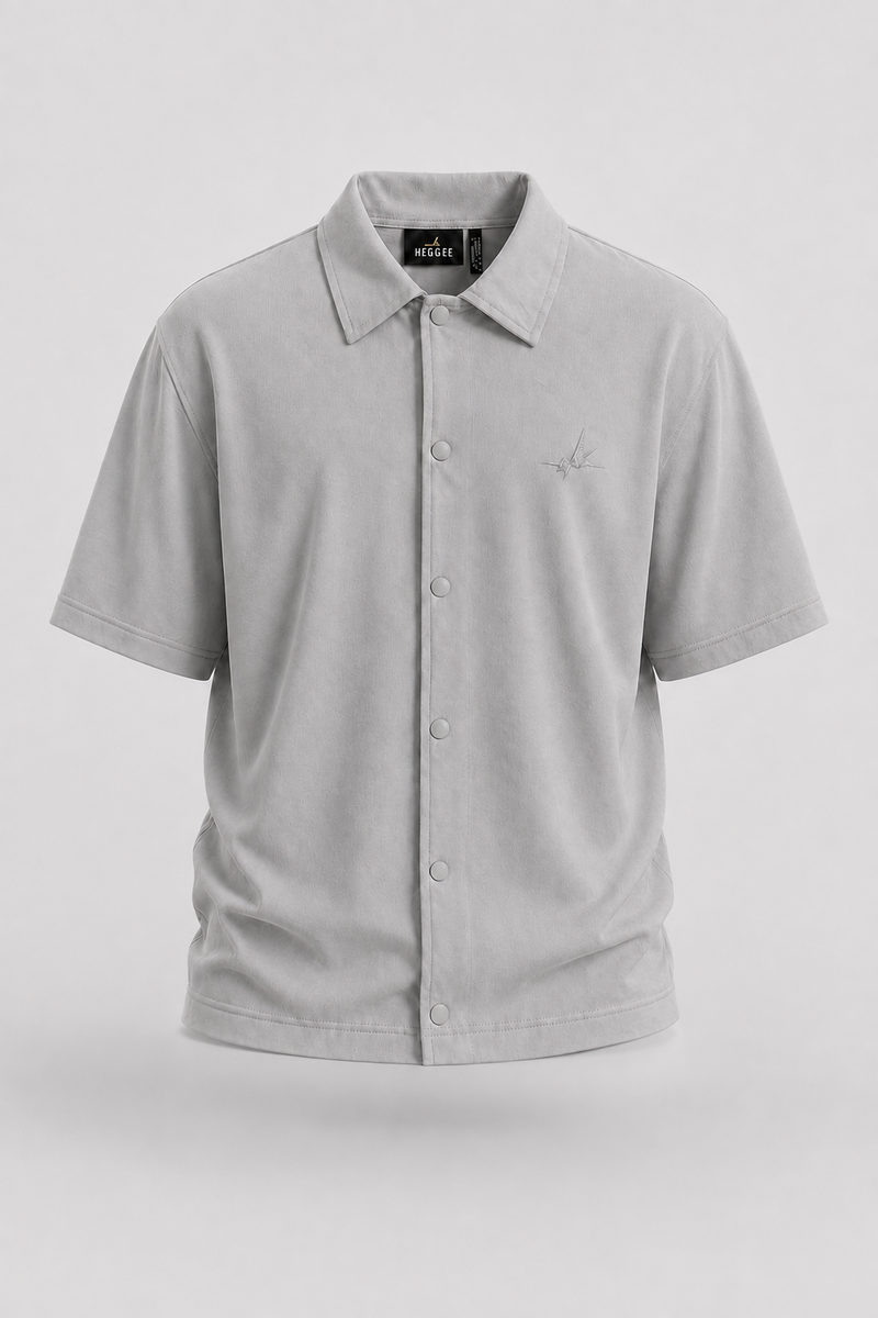 A light gray short-sleeve button-up shirt with a pointed collar and a small embroidered logo on the left chest, displayed on a neutral light gray background.