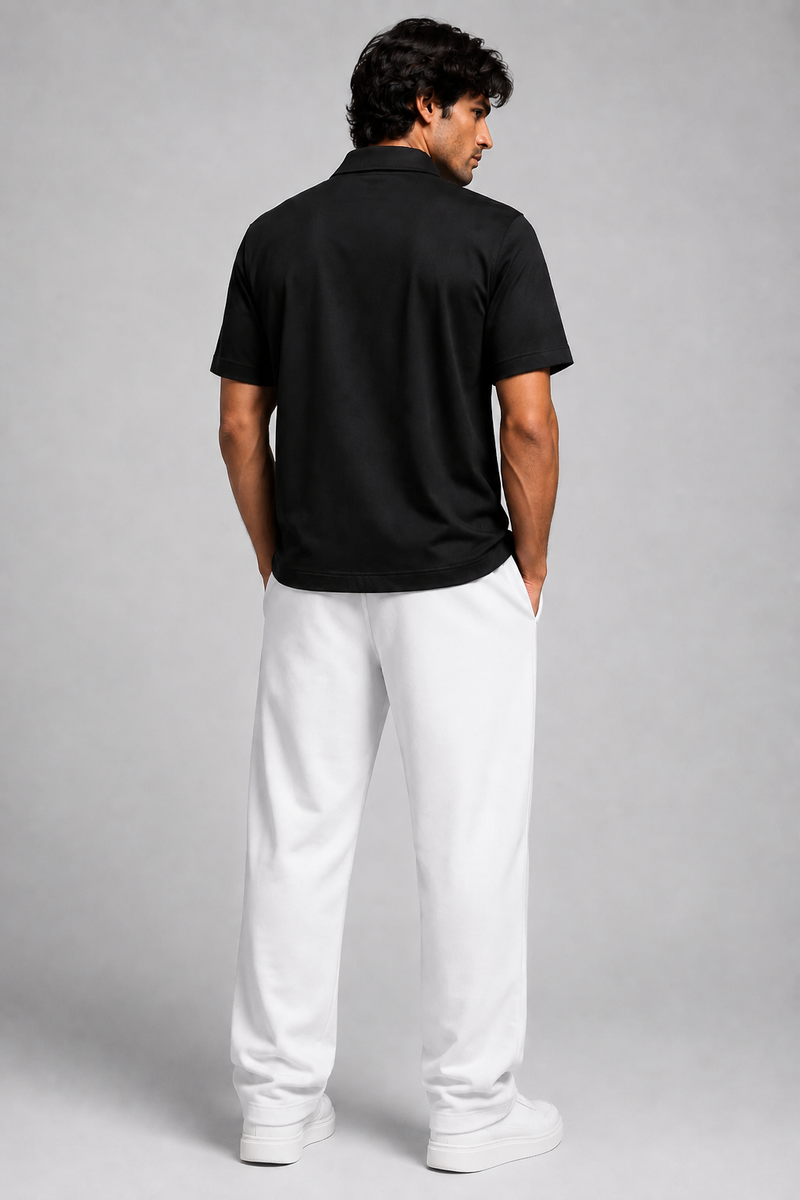 A man shown from the back wearing a black short-sleeve polo shirt and white trousers, standing against a light gray studio background.
