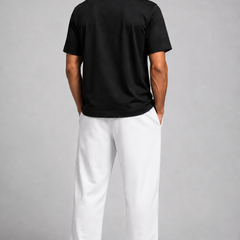 A man shown from the back wearing a black short-sleeve polo shirt and white trousers, standing against a light gray studio background.