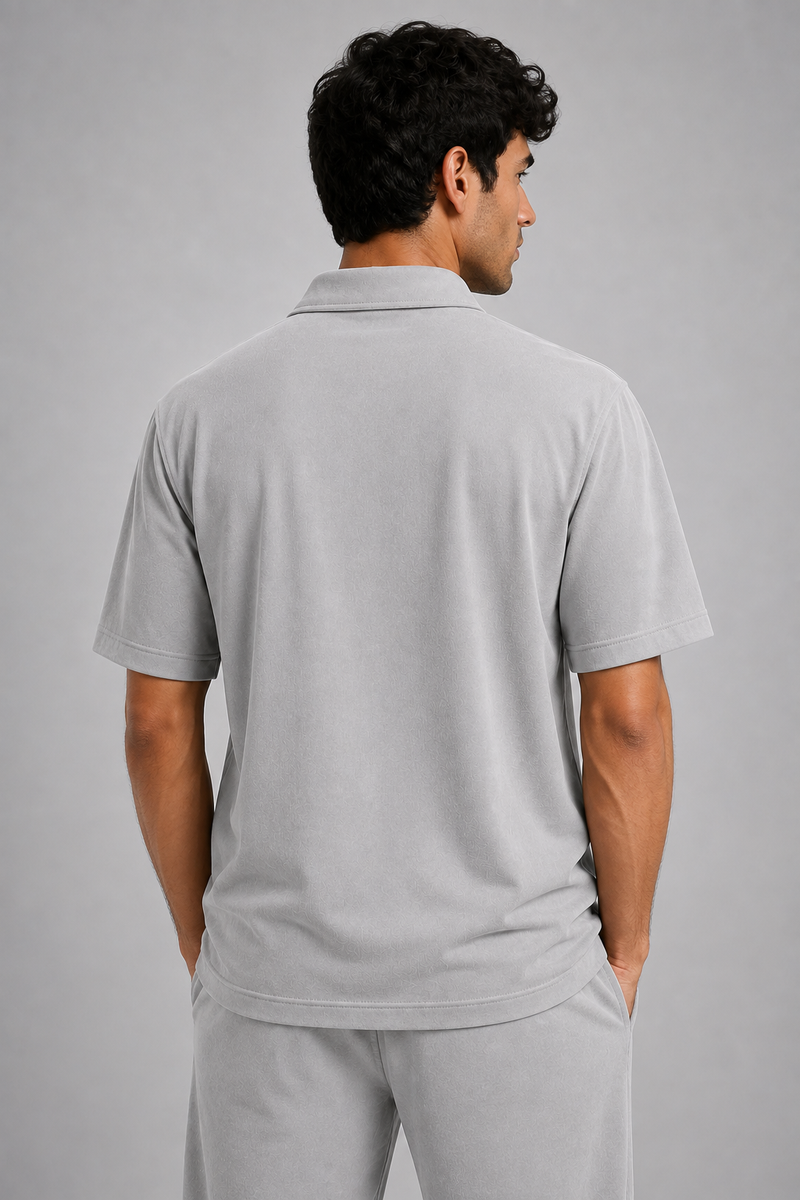 A man shown from the back wearing a light grey short-sleeve shirt and matching light gray pants against a solid gray studio background.