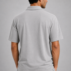 A man shown from the back wearing a light grey short-sleeve shirt and matching light gray pants against a solid gray studio background.