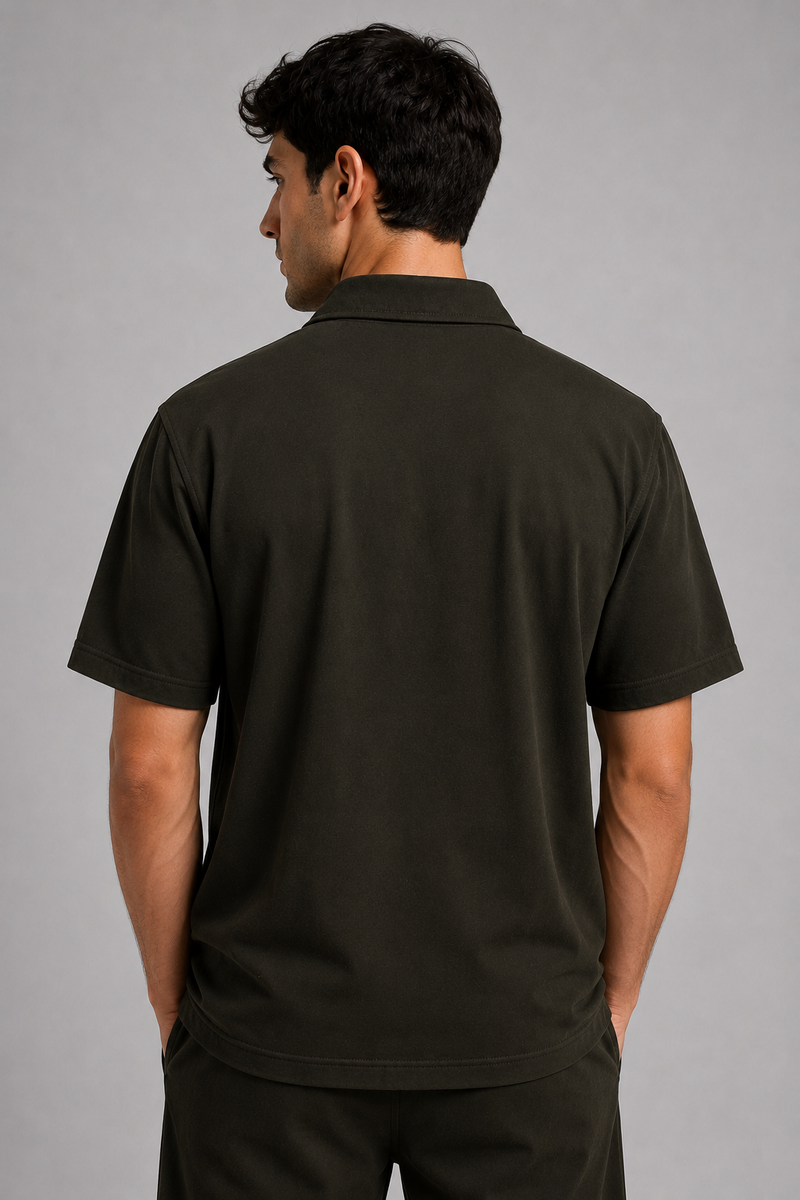 A man viewed from the back wearing a dark olive green short-sleeve shirt against a plain gray studio background.