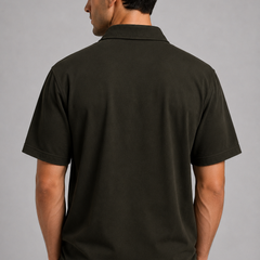 A man viewed from the back wearing a dark olive green short-sleeve shirt against a plain gray studio background.