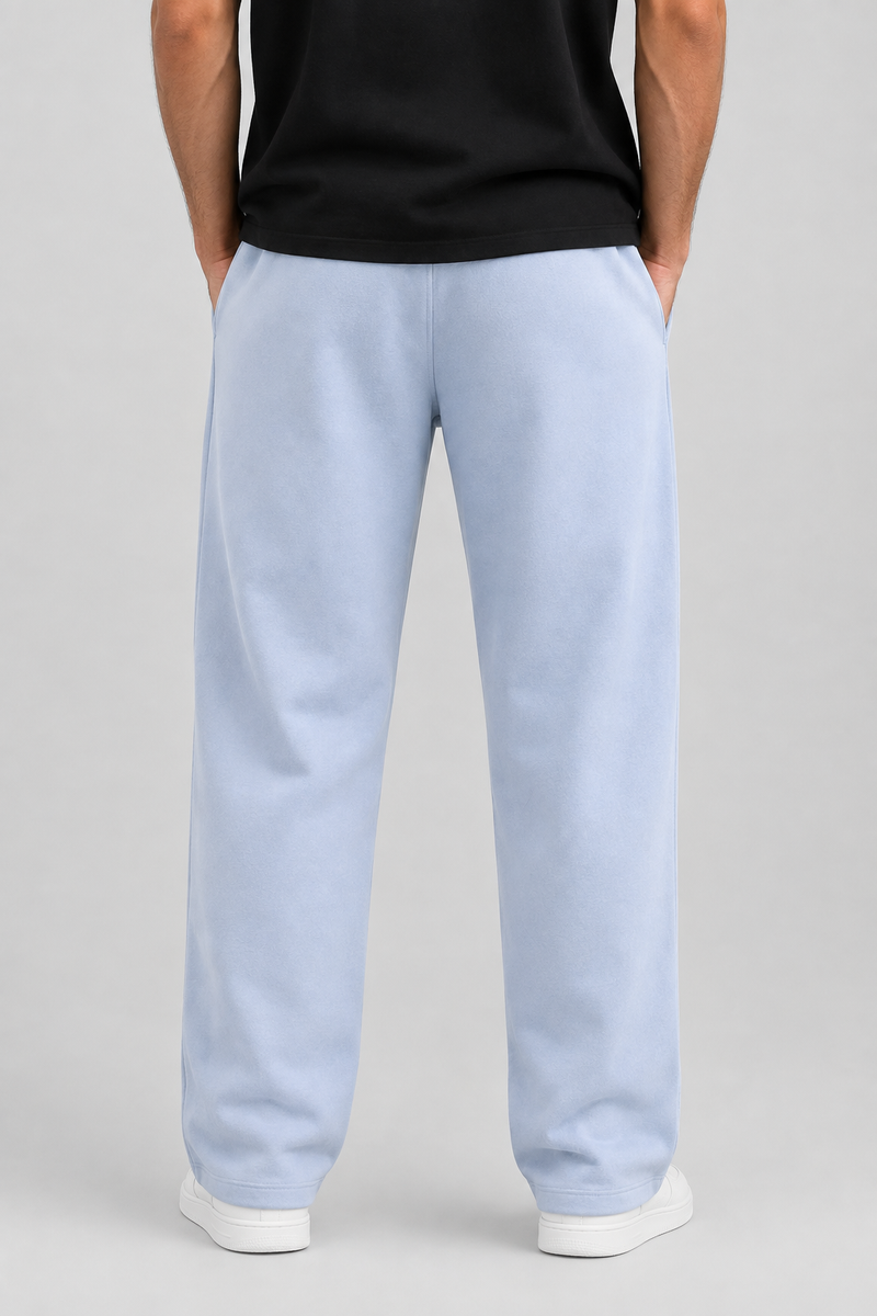A person shown from the back wearing light blue wide-leg sweatpants, a black t-shirt, and white sneakers against a neutral gray studio background.