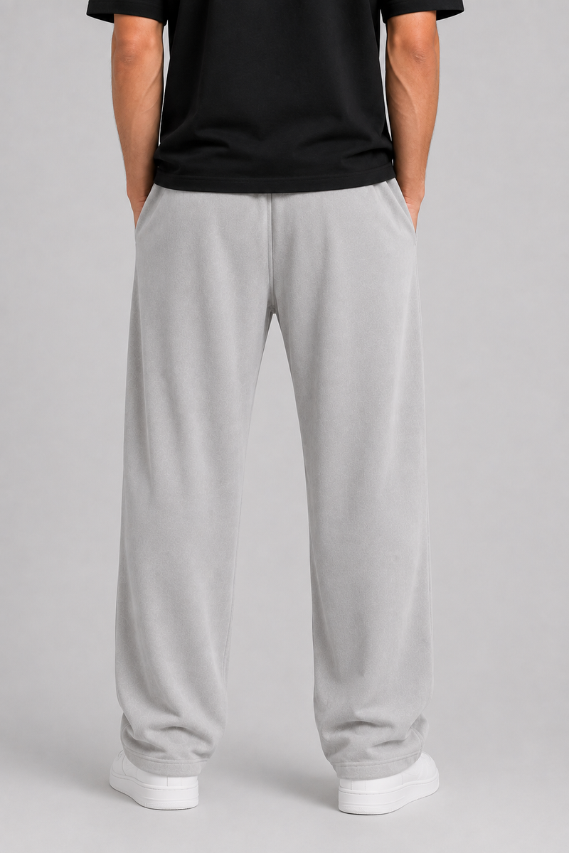 A person shown from the back wearing light gray sweatpants, a black t-shirt, and white sneakers against a neutral gray studio background.