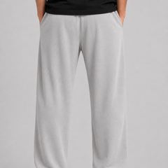 A person shown from the back wearing light gray sweatpants, a black t-shirt, and white sneakers against a neutral gray studio background.