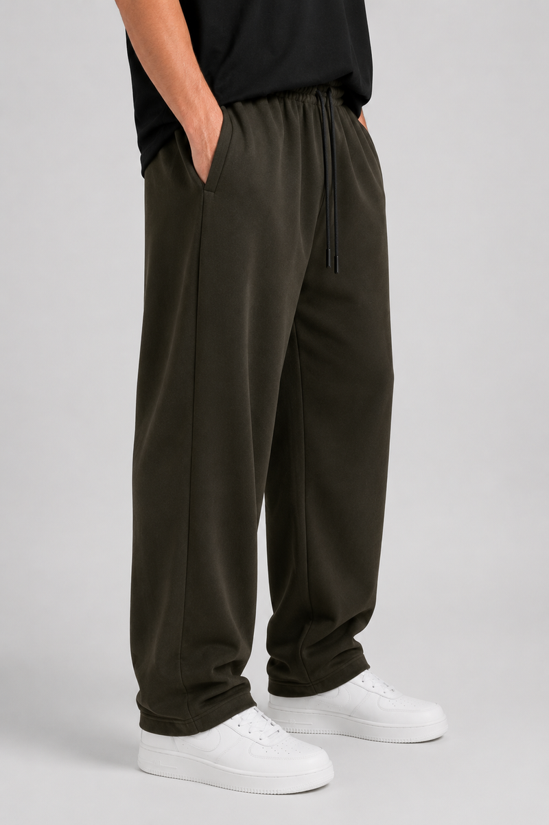 A person wearing dark olive green drawstring sweatpants with a black top and white sneakers, standing against a light gray studio background.