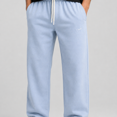 A person wearing light blue sweatpants with a white drawstring, paired with a black top and white sneakers, shown from the chest down against a light gray studio background.