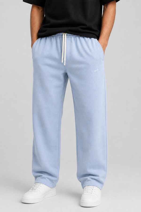 A person wearing light blue sweatpants with a white drawstring, paired with a black top and white sneakers, shown from the chest down against a light gray studio background.