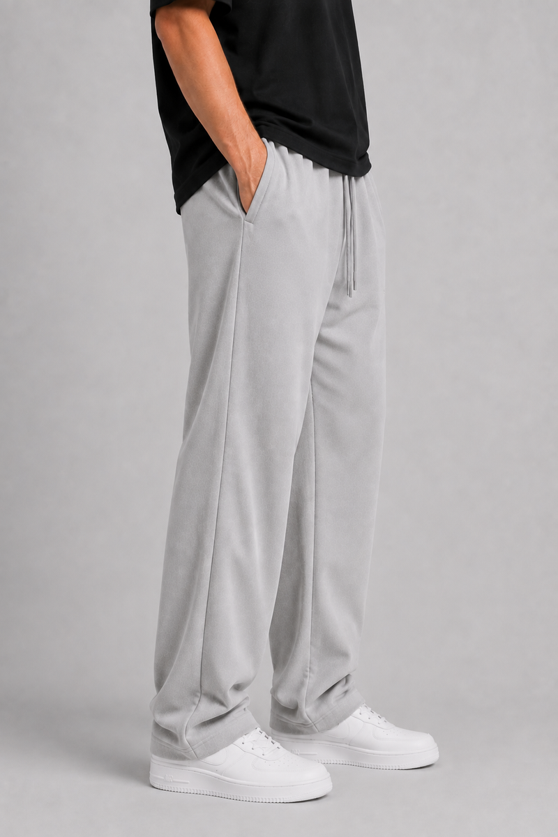 A person wearing light gray drawstring sweatpants, a black top, and white sneakers, standing against a plain light gray studio background.