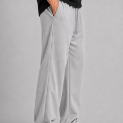 A person wearing light gray drawstring sweatpants, a black top, and white sneakers, standing against a plain light gray studio background.
