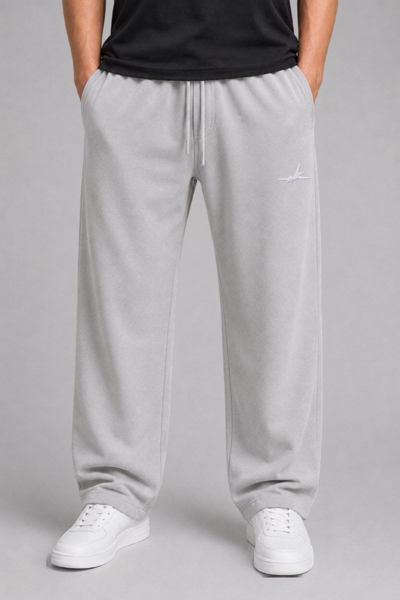A person wearing light gray sweatpants with a white drawstring, paired with a black top and white sneakers, shown from the waist down against a plain gray studio background.
