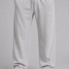 A person wearing light gray sweatpants with a white drawstring, paired with a black top and white sneakers, shown from the waist down against a plain gray studio background.