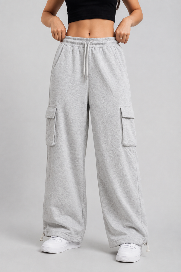 A person wearing light heather gray wide-leg cargo sweatpants with side flap pockets, a drawstring waist, and white sneakers, photographed against a plain light gray studio background.