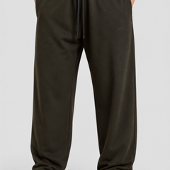 A person wearing loose dark olive green sweatpants with a drawstring waist, paired with a black top and white sneakers, shown from the waist down on a light gray studio background.
