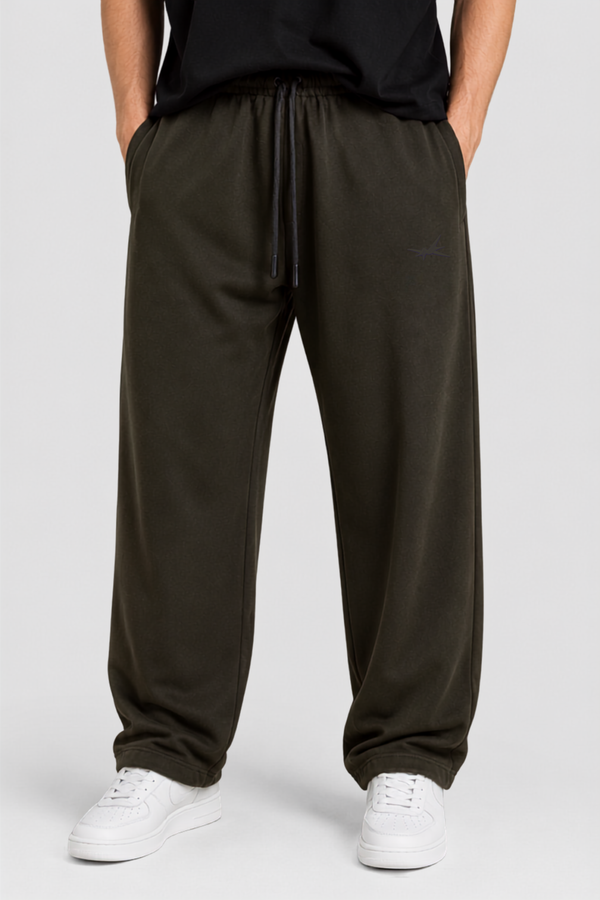 A person wearing loose dark olive green sweatpants with a drawstring waist, paired with a black top and white sneakers, shown from the waist down on a light gray studio background.