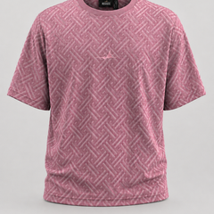 A pink short-sleeve crewneck t-shirt with a tonal geometric basketweave pattern and a small tonal logo on the left chest, displayed on a neutral light gray background.