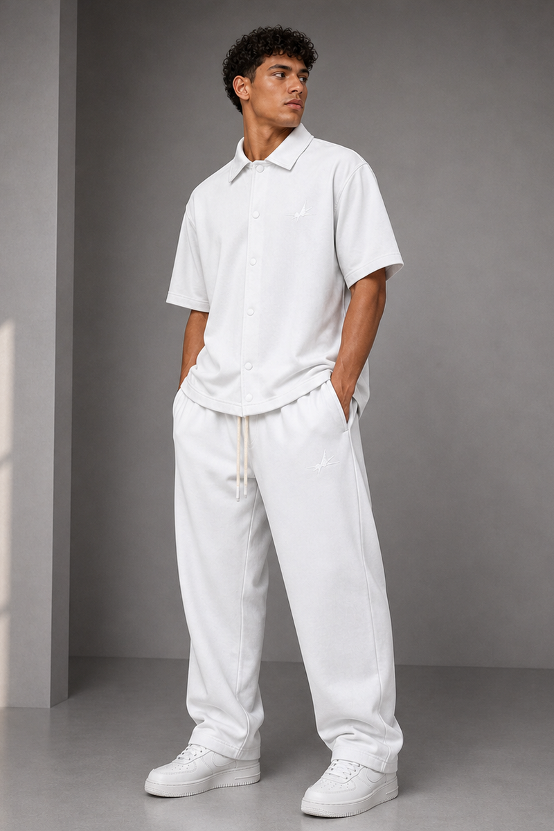Man wearing a white outfit standing against a gray wall with a light source casting shadows.