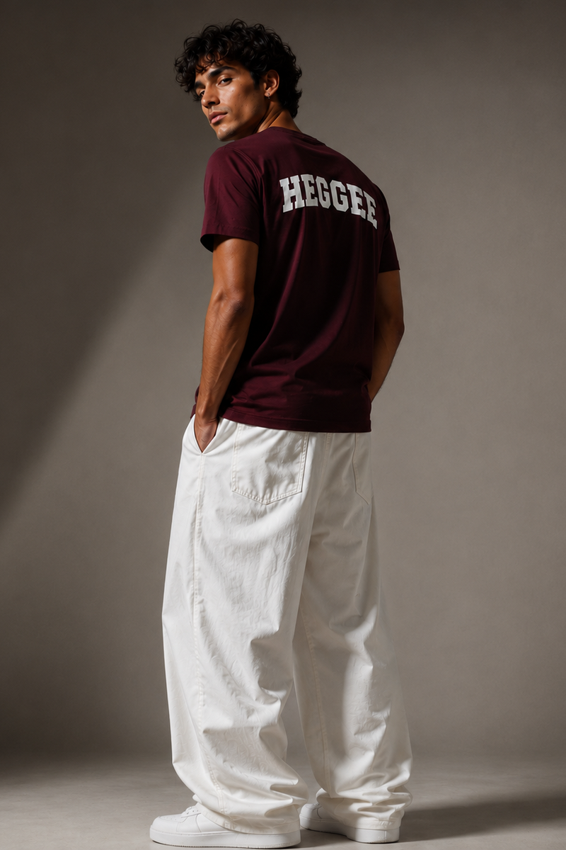 Man wearing a maroon 'HEGGER' t-shirt and white pants against a gray background