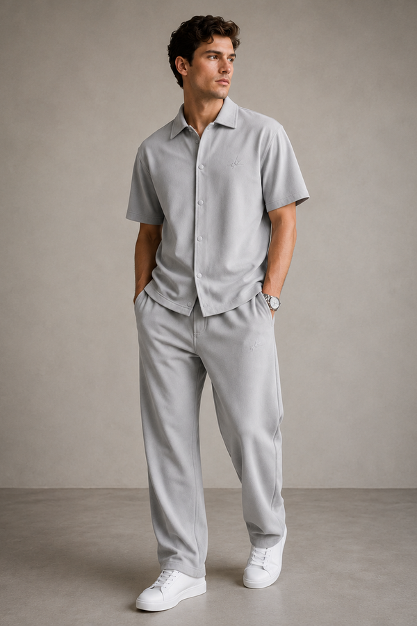 Man wearing a gray shirt and pants with white shoes against a plain background