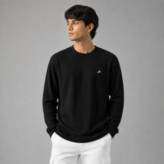 Man wearing a black long-sleeve shirt with a small logo on a gray background