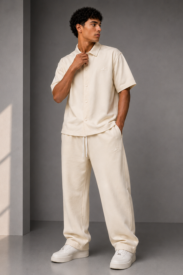 Man wearing a beige outfit standing against a gray wall with a light source casting shadows.